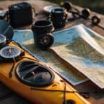 A kayak tour being planned with maps, compass, and gear spread out on a table