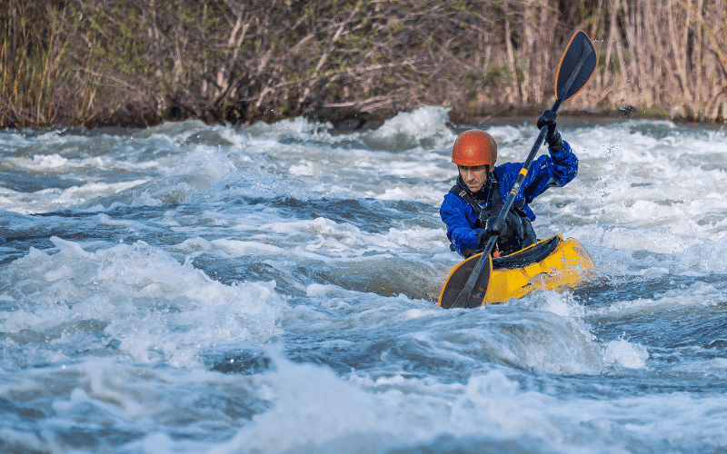 A kayaker paddling smoothly through clear waters, avoiding sharp rocks and navigating around obstacles to prevent sports injuries